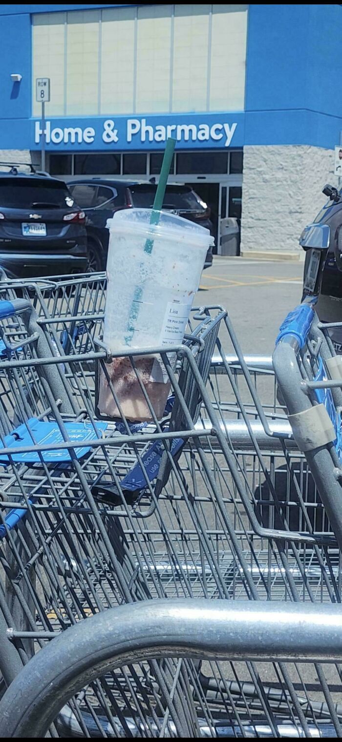 Empty Starbucks cup left in a shopping cart outside a Walmart Home and Pharmacy entrance in a parking lot.