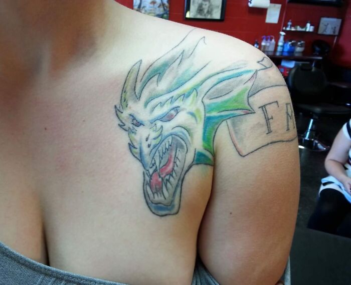 Dragon tattoo fail on a person's shoulder with uneven lines and awkward design, an example of epic tattoo fails shared online