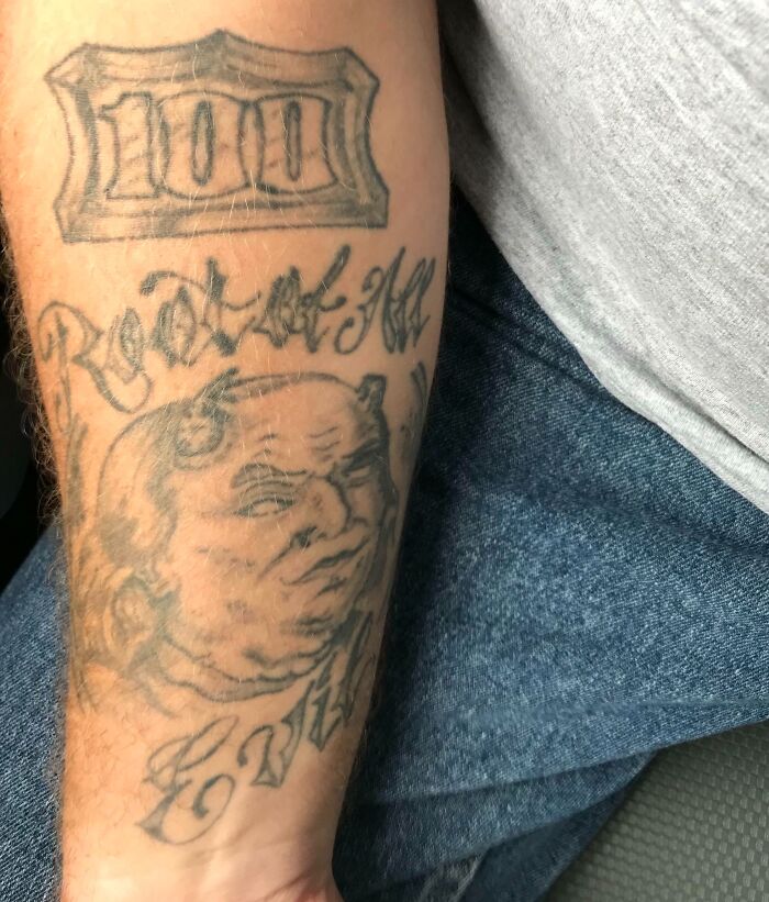 Close-up of an arm with a tattoo fail featuring a poorly drawn devil face and faded text on the forearm.