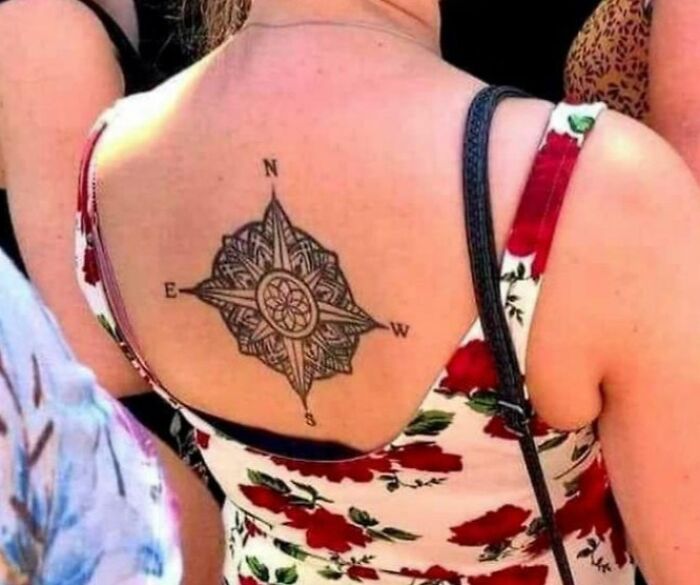 Compass tattoo with incorrect directions on a person's upper back wearing a floral dress, an epic tattoo fail shared online