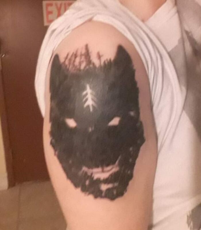 Tattoo fail of a poorly executed black wolf face with unclear details on a person's upper arm.