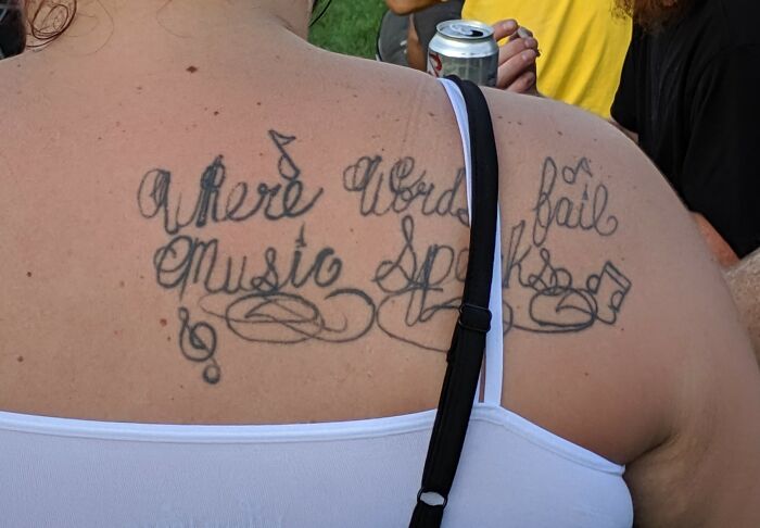 Tattoo fail on upper back with misspelled words and music notes, showcasing an epic tattoo fail shared by many.