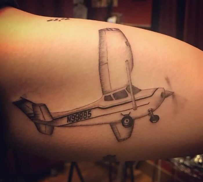 Tattoo fail showing a poorly executed airplane with uneven wings and inaccurate proportions on an arm.