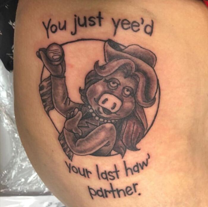 Tattoo fail featuring a cartoon pig dressed as a cowboy with the text "You just yee'd your last haw' partner."