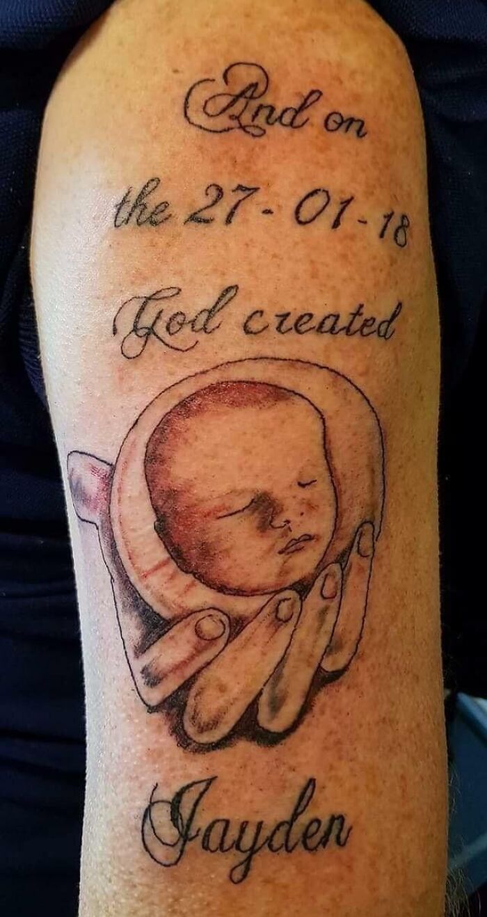 Tattoo fail of a hand holding a poorly drawn baby face with text including a date and name Jayden on arm.