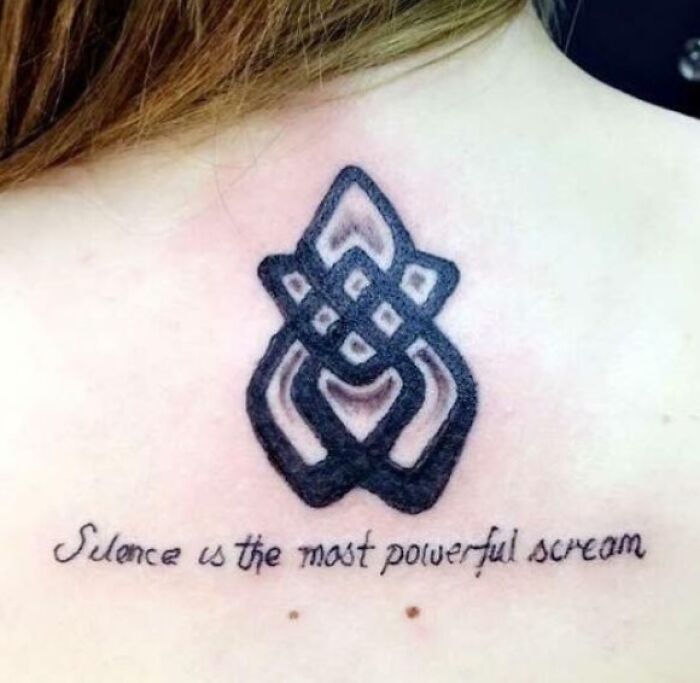 Close-up of a tattoo fail featuring a poorly drawn knot symbol and misspelled script on upper back.