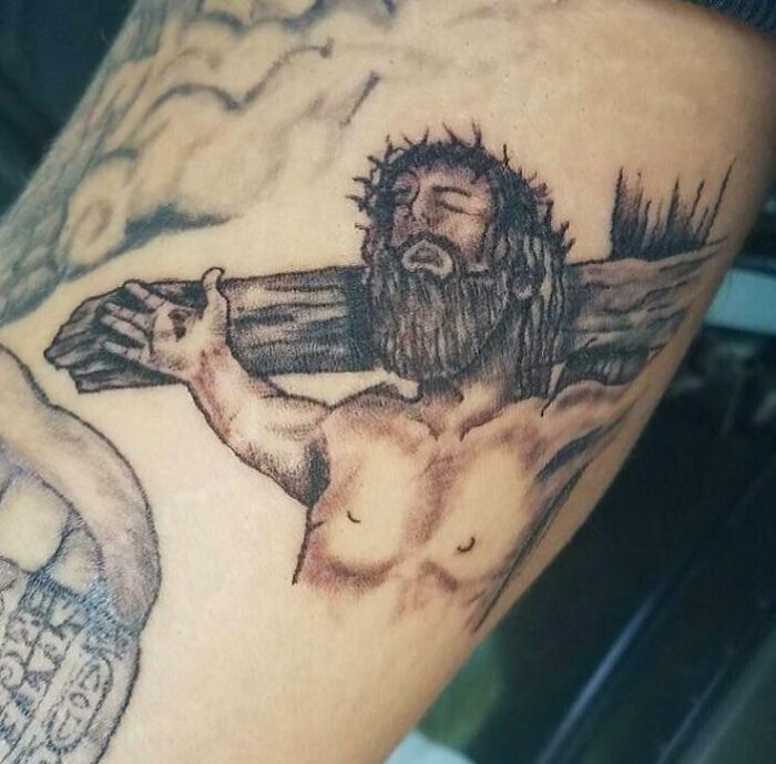 Tattoo fail of a poorly drawn crucifixion scene on arm showing a distorted figure with crown of thorns and outstretched arms.