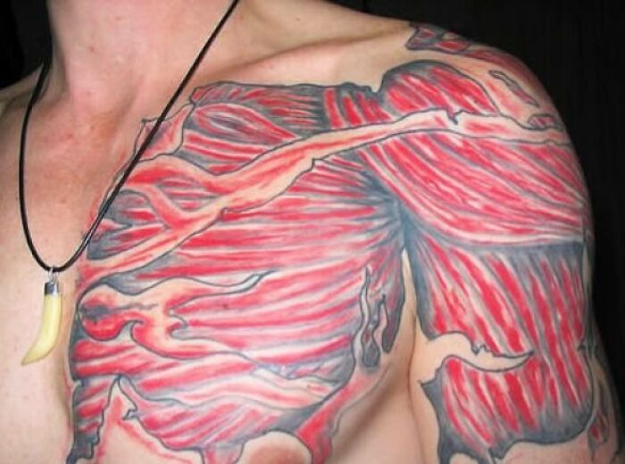 Red and black tattoo covering upper chest and shoulder with an unusual muscle-like design, a tattoo fail example.