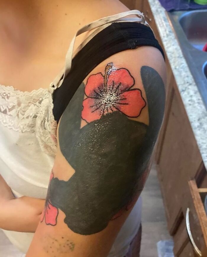 Tattoo fail showing a large black ink cover-up over a flower tattoo on an upper arm, part of epic tattoo fails collection.