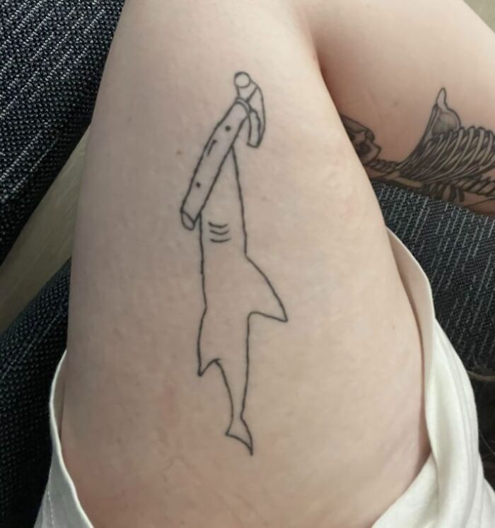 Minimalist line tattoo of a hammerhead shark on a person's thigh, an example of epic tattoo fails.