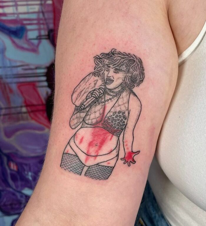 Tattoo fail of a singer with mismatched proportions and red ink smudges on upper arm, showcasing epic tattoo fails.