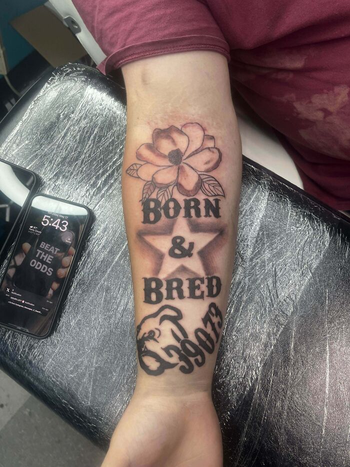 Tattoo fail on forearm featuring a flower, star, text born & bred, and a distorted dog face with numbers.