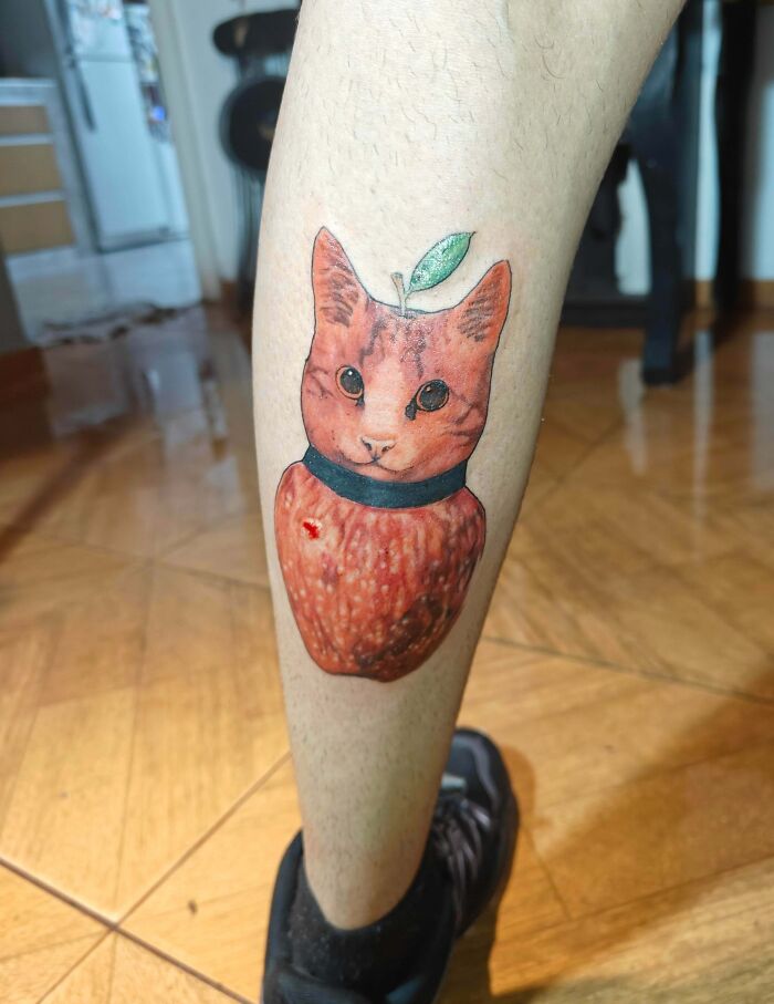Tattoo fail of a cat with an apple body on a person's lower leg, showcasing an epic and humorous tattoo mistake.