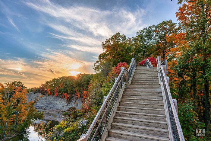 Wooden stairs surrounded by vibrant autumn leaf colors and fall foliage under a partly cloudy sky at sunset.