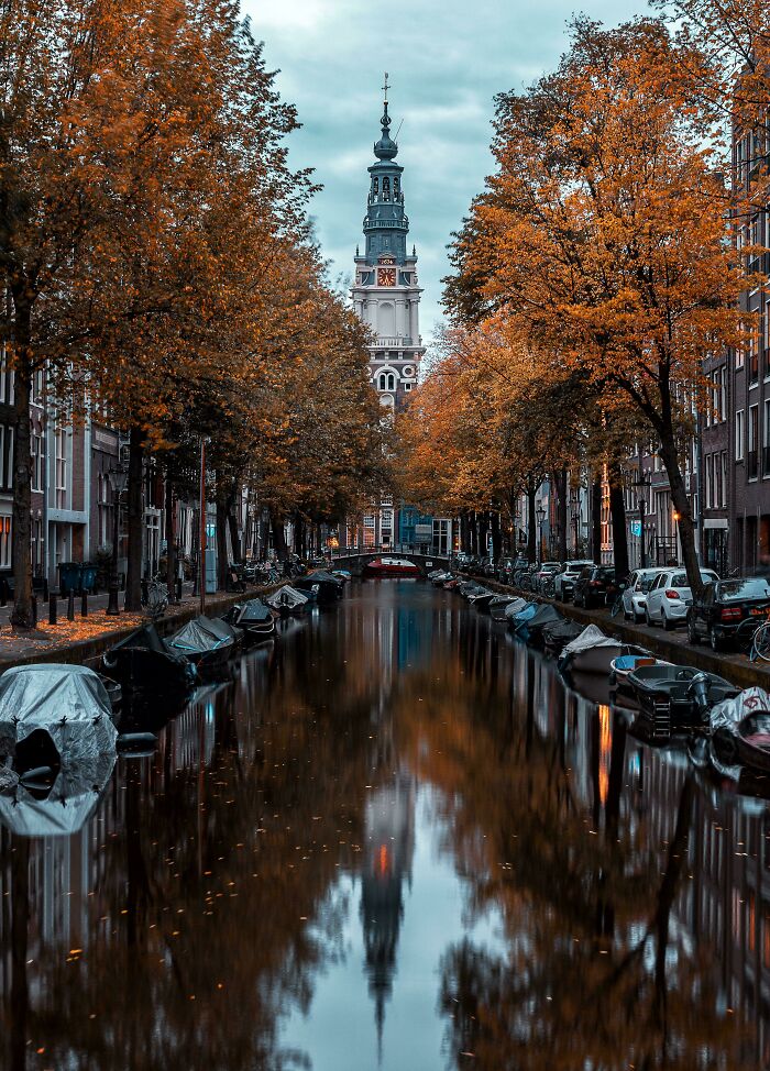 Canal lined with boats and trees showcasing vibrant autumn leaf colors reflected in the water during fall foliage season.
