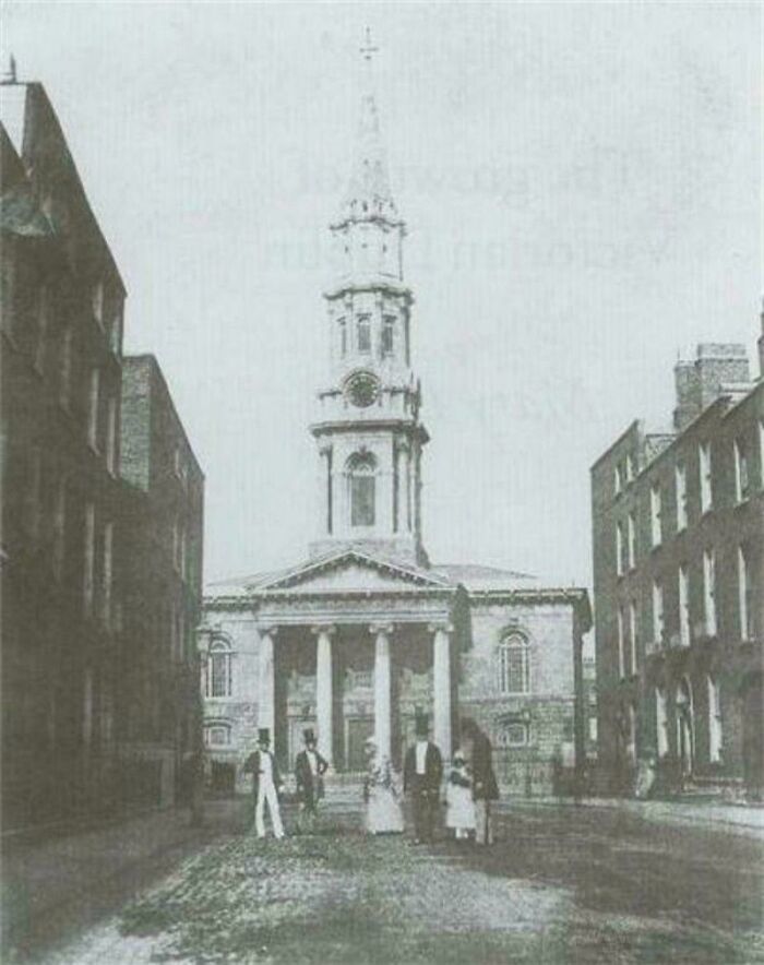 Historic black and white photo showing a world capital's old church and people in period clothing before modern times.