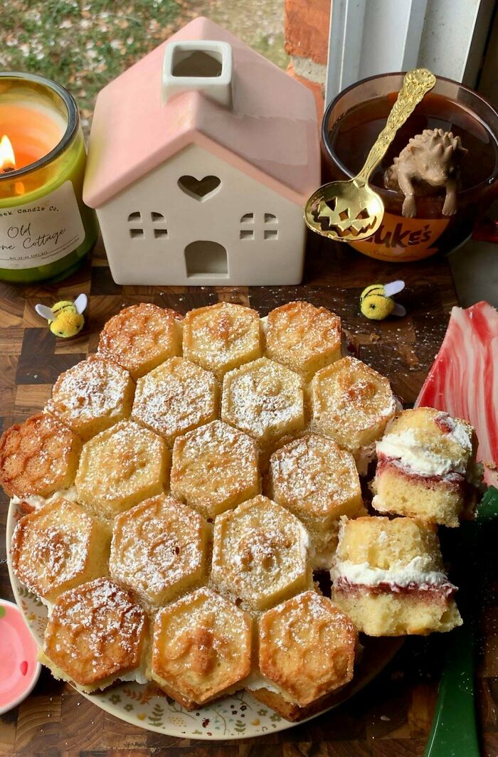 Hexagon-shaped baked treats with powdered sugar, a ceramic cottage, candle, and whimsical bee decorations showcasing cottage core aesthetics.