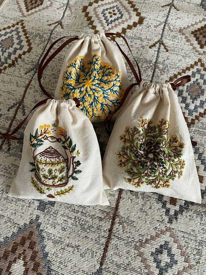 Three drawstring bags with floral and teapot embroidery, showcasing charming cottage core aesthetics on a patterned fabric background.