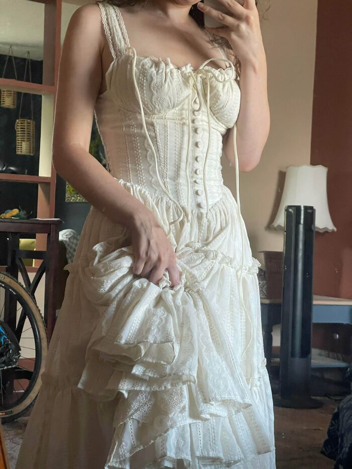 Woman wearing a cream lace dress with corset-style bodice, showcasing cottage core aesthetics in a cozy indoor setting.