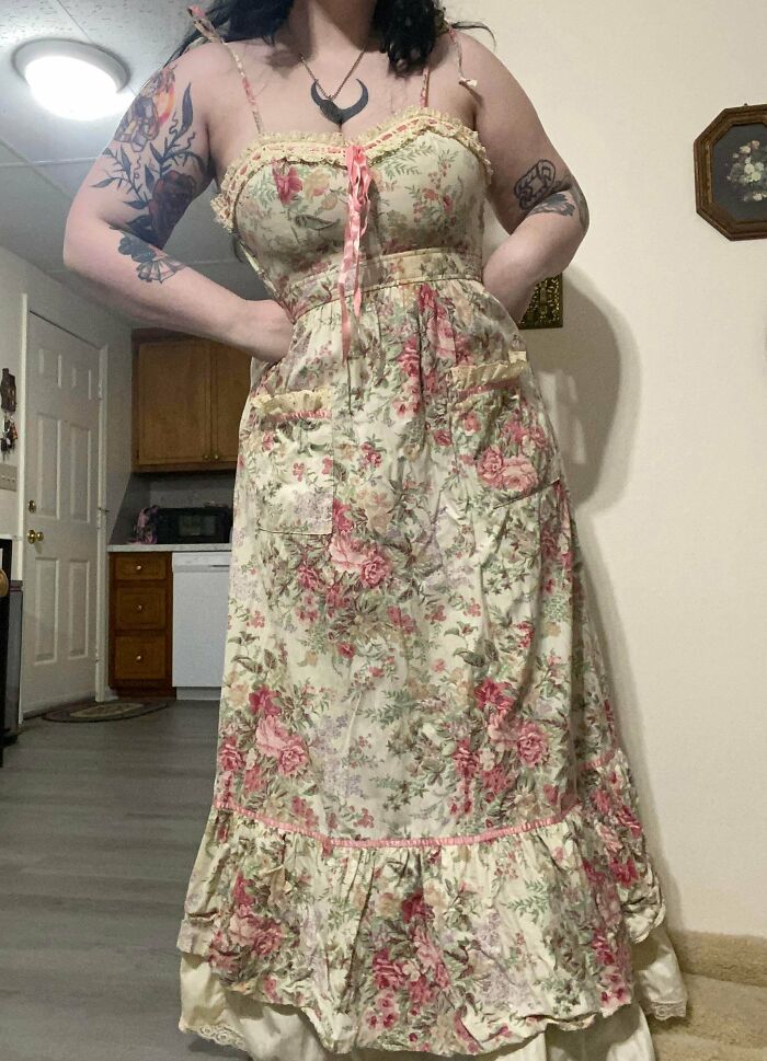 Person wearing a floral vintage dress in a cozy indoor setting showcasing cottage core aesthetics style.