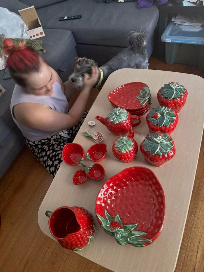 Person with red hair playing with dog beside table of strawberry-themed pottery, showcasing cottage core aesthetics in a cozy home setting