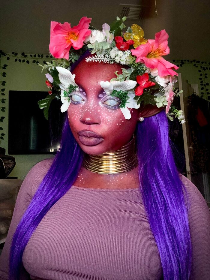 Woman with purple hair and floral crown showcasing whimsical cottage core aesthetics makeup and style indoors.