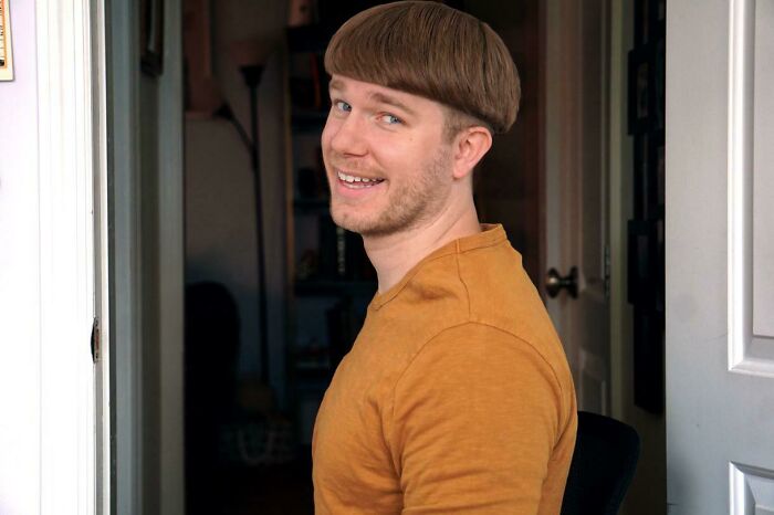 Young man with a humorous bowl haircut wearing a mustard shirt, showcasing a hilariously tragic hair accident indoors.