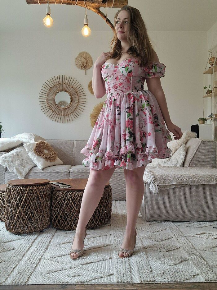 Woman in a floral dress posing in a cozy living room featuring cottage core aesthetics and natural decor elements.