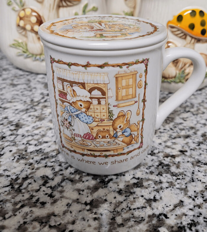 Ceramic mug with whimsical cottage core aesthetics featuring rabbits baking in a rustic kitchen scene on granite countertop.