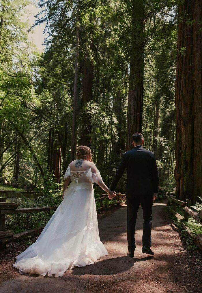 Couple holding hands walking through a sunlit forest path, embodying cottage core aesthetics in nature.