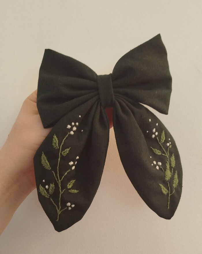 Black fabric bow with delicate green and white floral embroidery, showcasing cottage core aesthetics in a whimsical style.