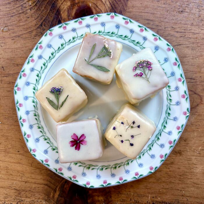 Small square cakes with white icing and edible flowers on a floral plate showcasing cottage core aesthetics.
