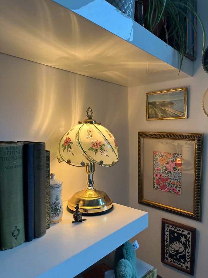 Vintage floral lamp on white shelf with books and framed art, showcasing cozy cottage core aesthetics in home decor.