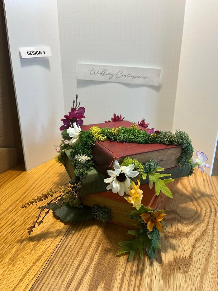 Stack of vintage books decorated with moss and wildflowers, showcasing a rustic cottage core aesthetic centerpiece design.