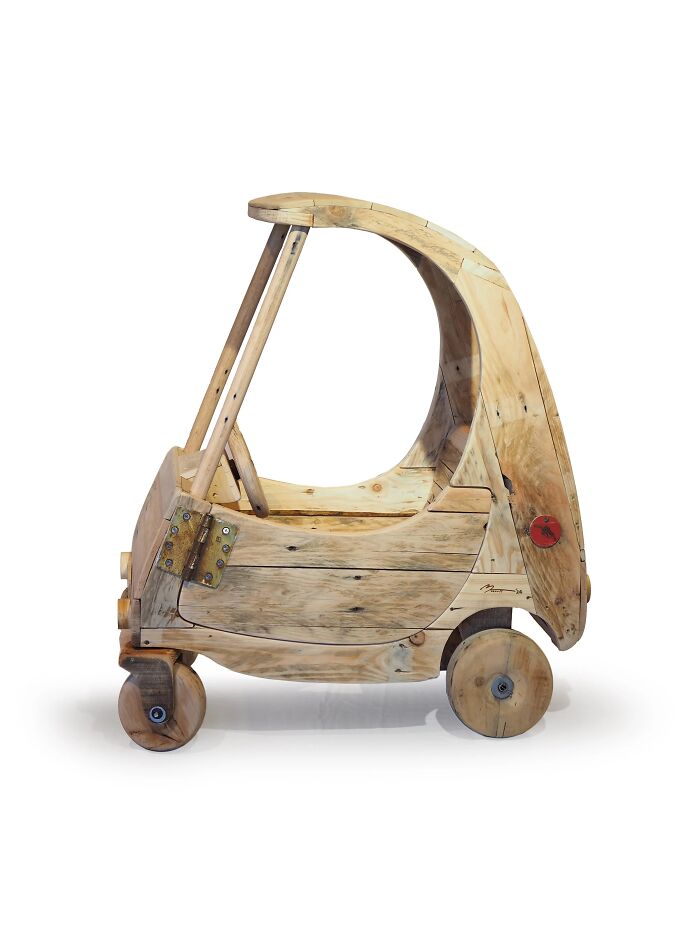 Wooden toy car sculpture made from recycled materials showcasing witty commentary on modern life and waste.
