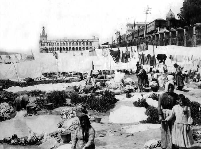 Black and white photo showing daily life with people washing clothes outdoors in an early world capital city before modern times