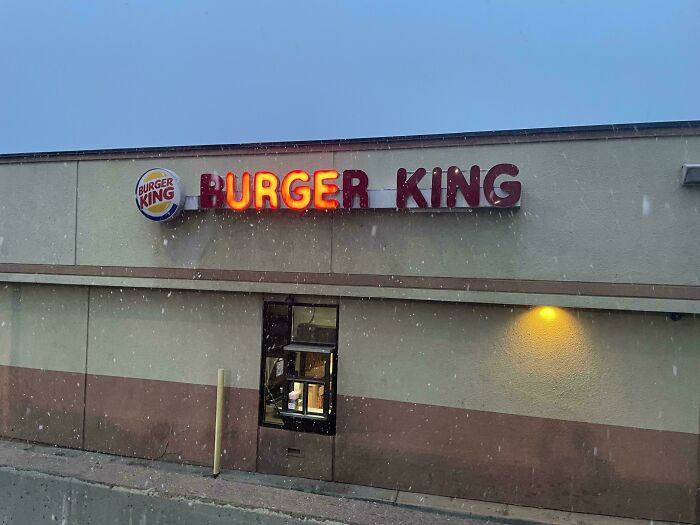 Burger King LED sign with partially lit letters on building exterior during snowfall at dusk.