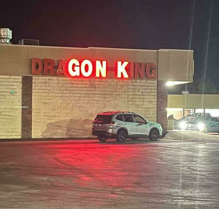 Partial LED sign reading dragon king with some letters lit in red, parked car reflecting the red light on the pavement at night