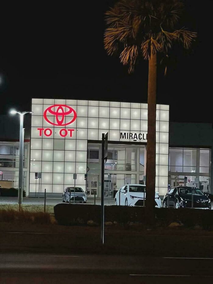 LED sign at a car dealership with illuminated panels and a partially lit brand logo visible at night.