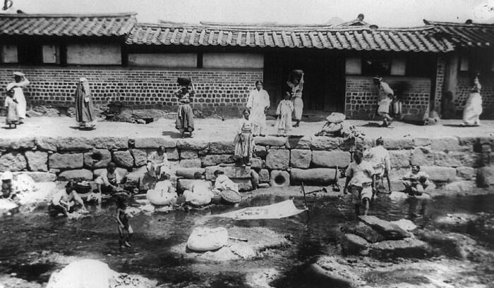 Black and white photo showing daily life in a historic capital city with people by a stone waterway before modern times.