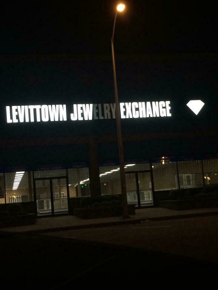 LED sign for Levittown jewelry exchange with a bright diamond icon, partially obscured by a street lamp at night.