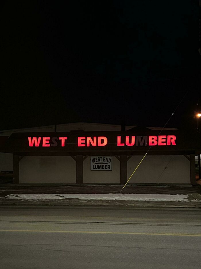 Red LED sign displaying West End Lumber on a building at night along a snowy roadside.