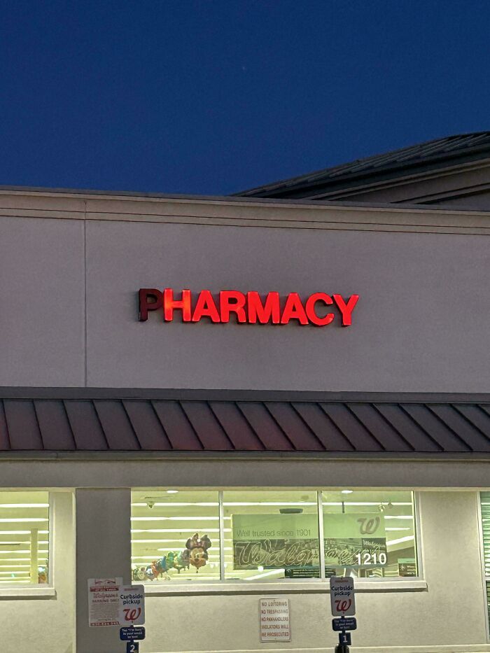 Red illuminated LED pharmacy sign on a building exterior against a dark evening sky.