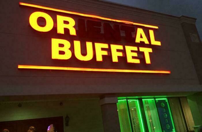 LED sign for an Oriental buffet with partially unlit letters glowing in bright yellow and orange hues at night.