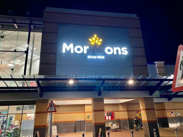 LED sign for Morrisons supermarket illuminated at night on the building facade, showcasing bright store branding.
