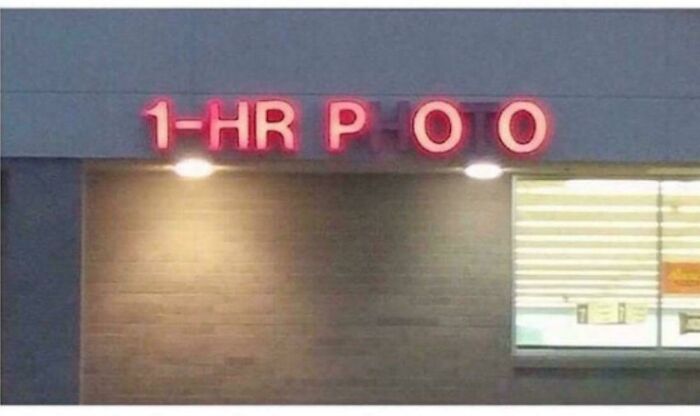 Faded LED sign with missing letters showing 1-HR P O O above a lit window on a building exterior at night.