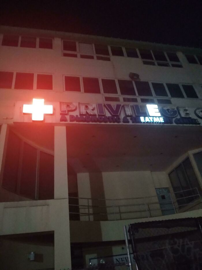 LED signs glowing at night on a building facade displaying a red cross and partial business name Privilege.