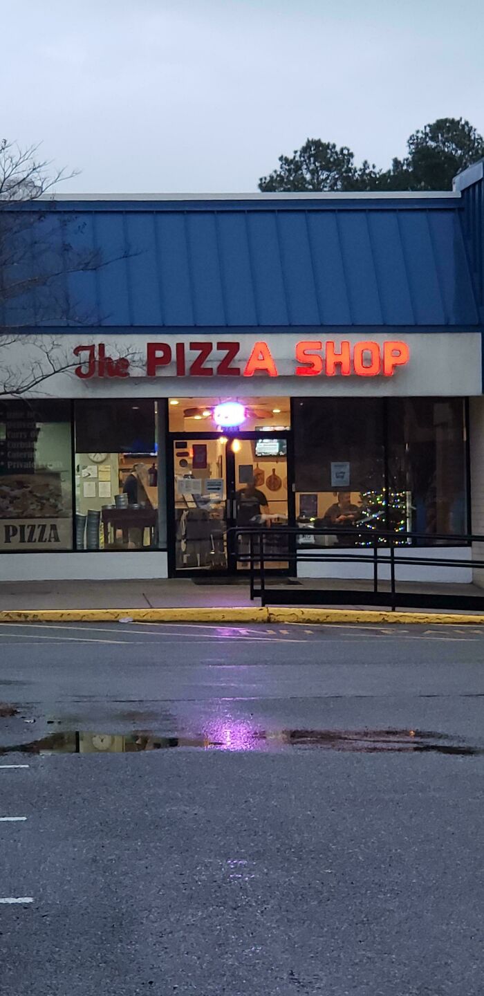 LED pizza shop sign glowing red above entrance of a small local restaurant during early evening hours.