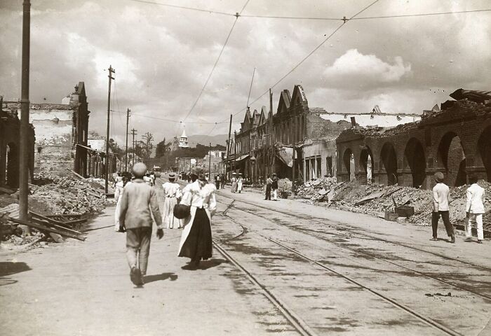 Street scene with people walking amidst ruins and damaged buildings showcasing the world's capitals before modern times.