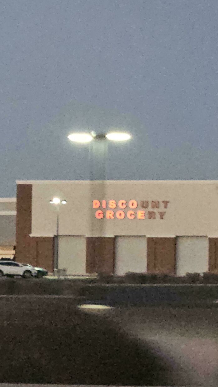 Faded LED grocery store sign at dusk with incomplete letters visible under bright street lights.